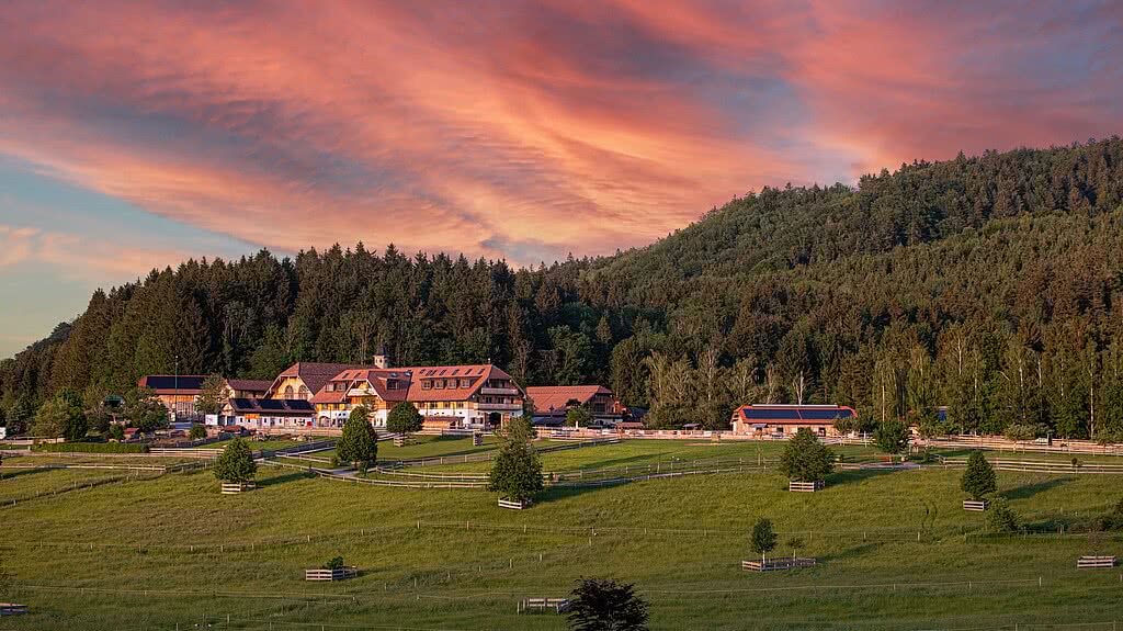 Außenanlage des Gute Aiderbichl im Sonnenuntergang mit idyllischer Lage am Waldrand umgeben von Natur